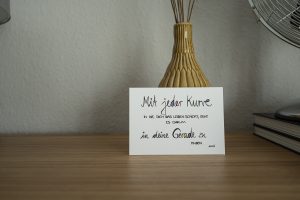 weiße Postkarte mit bunter Schrift "Mit jeder Kurve, in die dich das Leben schickt, geht es darum, in deine Gerade zu finden."