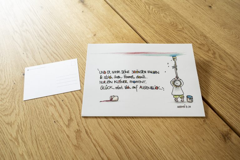 weiße Postkarte mit bunter Schrift "Und er nahm seine schönsten Farben & strich ihren Himmel damit. Nur ein kleiner Moment. Glück reimt sich auf Augenblick."