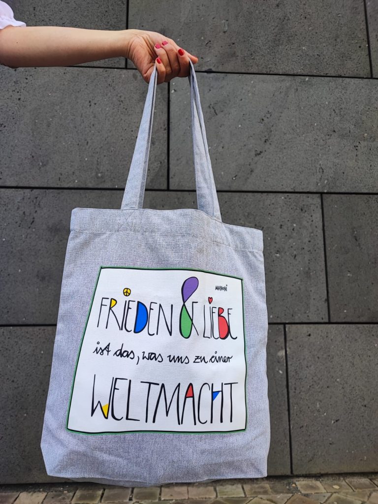 grauer Stoffbeutel mit bunter Schrift "Frieden & Liebe ist das, was uns zu einer Weltmacht"