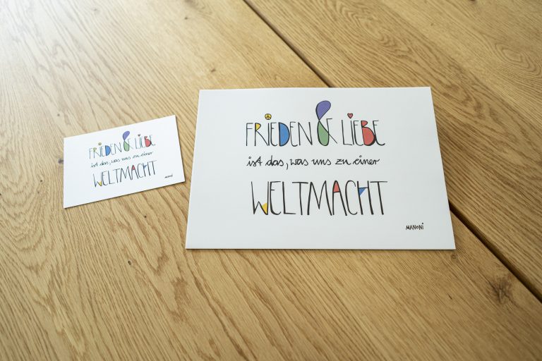 weiße Postkarte mit bunter Schrift "Frieden & Liebe ist das, was uns zu einer Weltmacht"